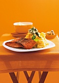 Salmon with basil, butter and mashed potatoes on plate against orange background