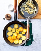 Two pans with roasted potatoes and onions on kitchen table