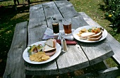 Gedeckter Tisch für 2 Personen: Chips, Sandwiches, Salat; draußen
