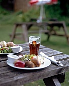 Salad, cheese and rolls on plate with glass of beer on wooden table