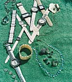 Schmuck und Uhren auf gruenem Sand aufgebreitet