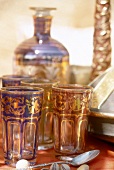 Orientalische Teegläser, bunt bemalt dahinter Karaffe aus Glas