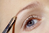 Close-up of gray eyed woman plucking her eyebrows