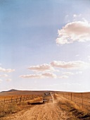 View of sky and old pickup truck moving on dirt track past the fields