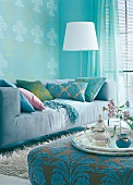 Interiors of room with blue sofa, turquoise patterned cushions and lamp