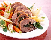 Close-up of rolled shoulder of lamb stuffed with herb, carrots and fennel bulbs on plate