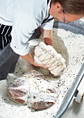 Metzger hebt ein Stück Schinken aus der Salz-Gewürz-Mischung, nah