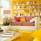 White couch with pink cushions and small table with flower vase in living room