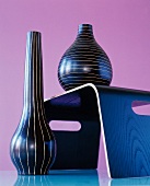 Two black vases with horizontal and vertical white stripes on floor and black table