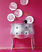 Silver chest with vase and plates as wall hanging on pink wall