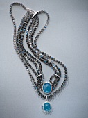Multi-row black beads chain with blue stone on gray background