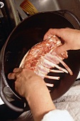 Close-up of raw suckling pig being placed in pan