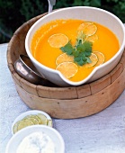 Carrot and coriander soup with lemon slices and coriander leaves in bowl