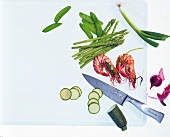 Different varieties of raw vegetables and knife on a chopping board, overhead view