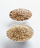 Two bowls filled with rye flakes on white background