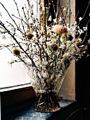 Close-up of branches and cherry blossoms in glass vase on windowsill