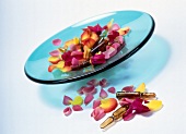 Ampoules and rose petals of different colours on blue glass bowl on white background