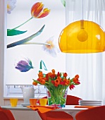 Fensterrollo mit Blumen, davor Tisch mit Tulpen