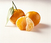 Zwei ganze Orangen mit Blatt und eine geschälte Orange