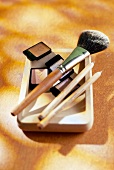 Eye shadow, pencil lip liners and powdered brush kept on wooden bowl