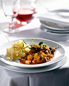 Duck stew with winter vegetables and noodles on plate and red wine