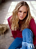 Portrait of pretty blonde woman with wavy hair wearing pink top and jeans sitting on floor
