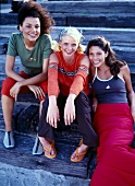 Portrait of three beautiful women in casual sitting on wooden surface and smiling