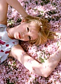 Portrait of pretty blonde woman relaxing on rose petals scattered on ground in sunlight