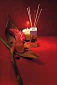 Lighted aroma candle, essence sticks, perfume bottle and flowers on red background