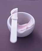 Close-up of white bowl and spatula with pink cream on purple background