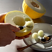Melon being gouged out with melon baller and placed in white bowl