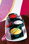 Colourful vegetable soup in three black bowls on tray with spoon