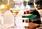 Close-up of glass of white wine, several bottles of wine and a corkscrew on table