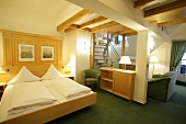 Bedroom with bed, cushion, chairs, table and stairs in hotel, Germany