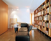 Brightly lit living room with black leather sofa, bookcase and wardrobe