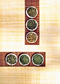 Six varieties of green tea on small white plates, overhead view