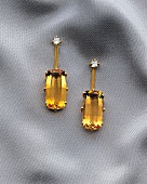 Close-up of gold earrings with citrin and diamond on gray fabric