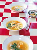 Soup bowls with chicken broth and grated pasta on checked table