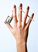 Woman's hand with red nail polish, holding top coat and tooth picker between fingers