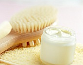 Skin cream and a massage brush on yellow towel