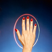 Close-up of woman's hand wearing red painted fingernails in a colourful circle