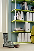 Shelf in green against blue wall and rubber boots in foreground on floor