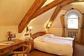 Bedroom with bed, cushion, chairs and table in attic of hotel, Germany
