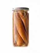 Closed glass jar with sausages on white background