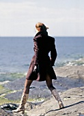 Frau im braunen Mantel macht Spaziergang am Meer.