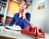 Woman wearing blue shirt talking on red old fashioned phone, blur