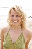 Portrait of beautiful blonde woman wearing green halter top standing on beach, smiling