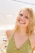 Portrait of beautiful blonde woman wearing green halter top standing on beach, smiling