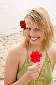 Happy blonde woman with flower in hair in green halter top holding flower on beach