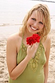 Woman wearing green halterneck dress holding red flower on beach, laughing